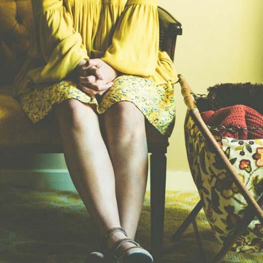 A photo of a girl dressed in yellow sitting next to a container of knitted articles of clothing